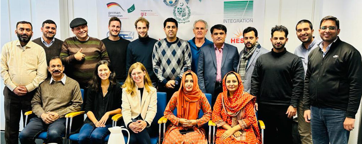 Das Bild zeigt die pakistanische Delegation gemeinsam mit den RLI Expert*innen für ein Gruppenbild aufgestellt, im Hintergrund ein Plakat mit Logos
